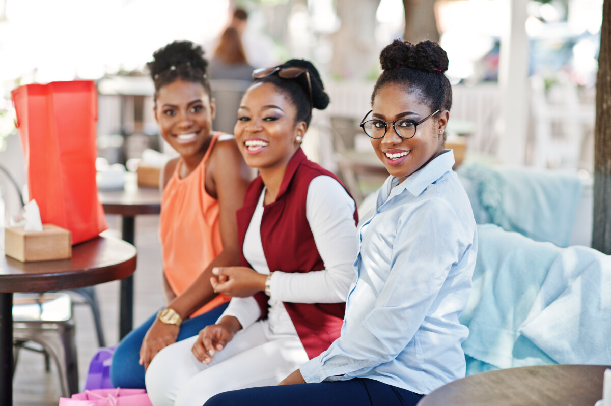 Three casual african american girls with colored shopping bags w